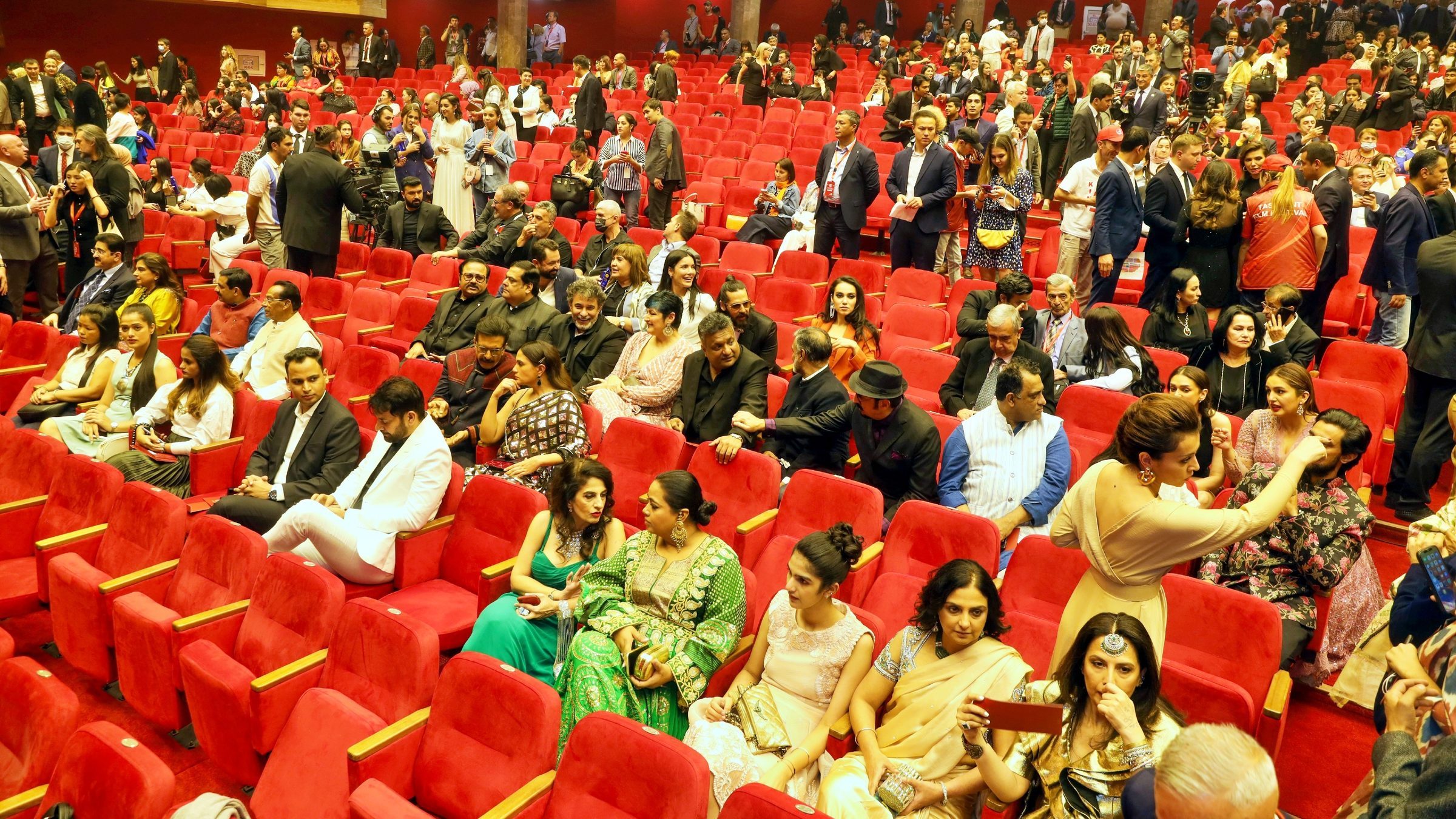 Lithvik Mukesh Sharma attends the Tashkent Film Festival. A large enclosed auditorium with tiered rows of red velvet upholstered seats holds dozens of attendees. A red illuminated EXIT sign is visible